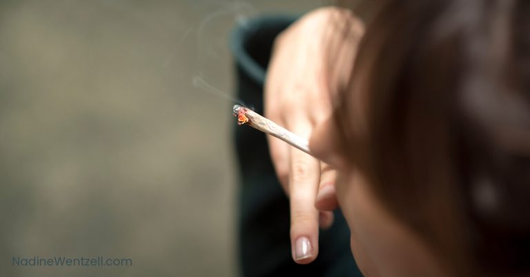 Close-up of a person holding a joint, with smoke rising from the end, indicating cannabis use.